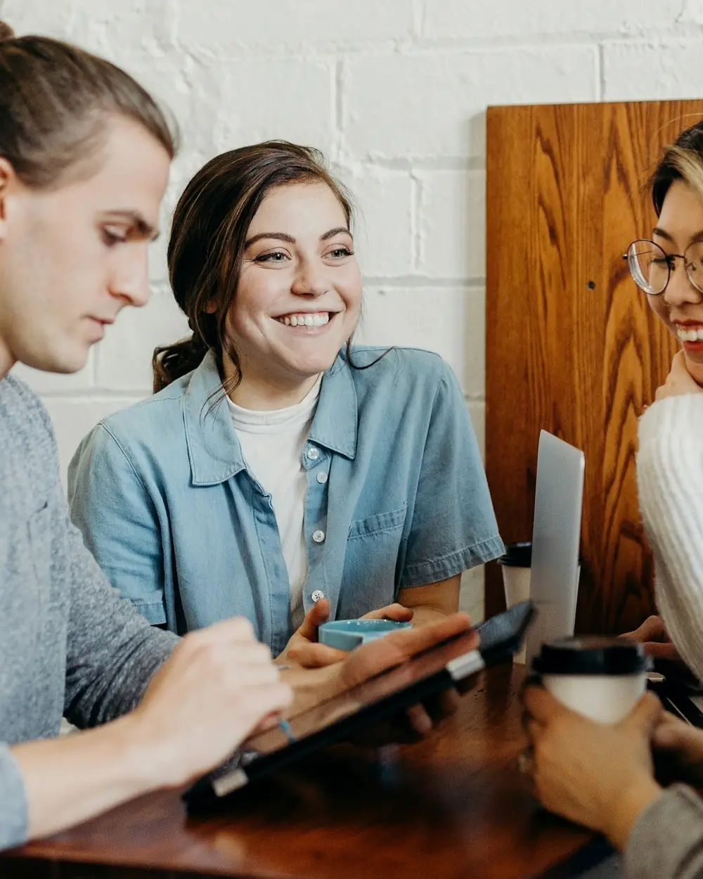 Team of four collaborating around a table with a tablet and laptop in a bright office